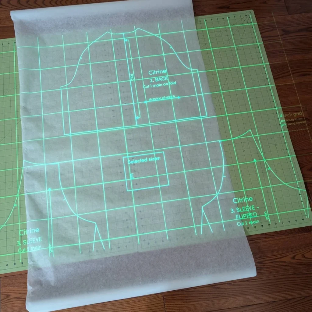 Projected sewing pattern aligned to grid lines on a cutting mat before cutting.